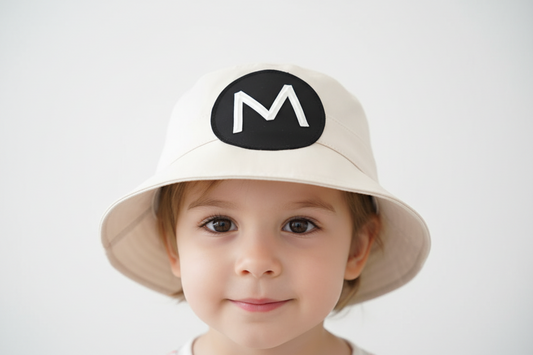 Beige bucket hat with a black circle featuring the letter 'M' on a light gray background