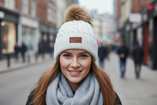 White knit beanie with a brown faux fur pom-pom on a white background